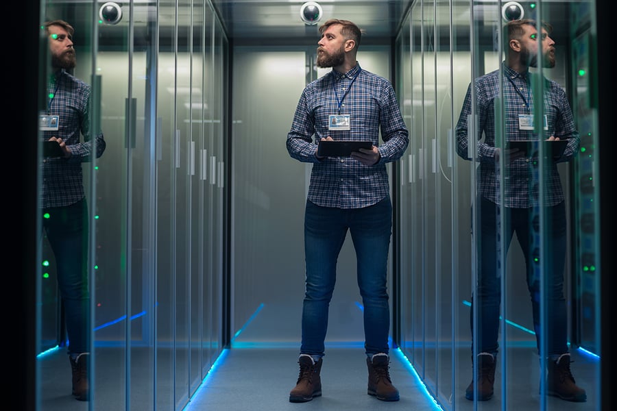 A cybersecurity expert on a tablet in a room full of computer servers