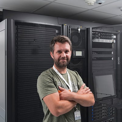 A pleased IT professional poses in front of a row of computer servers