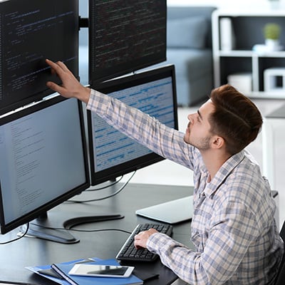 A man sits in front of a array of computer monitors